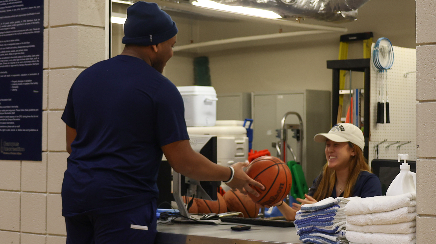 A CRC equipment issue student staff hands a basketball to a client.