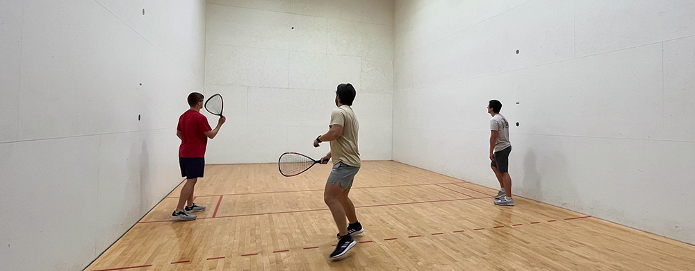 Three guys playing at the CRC squash court.